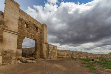 Photo of historic Harran University gates. Photo taken with wide angle lens from side. Enterance of the gate in front, with dusty roar aproaching to gate. Blue sky with clouds in the background.