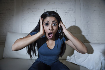 Naklejka premium latin woman at home sofa couch in living room watching television scary horror movie or suspense thriller