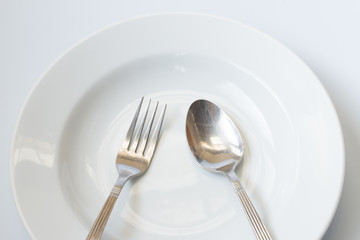 White dish with metal spoon and fork on gray background