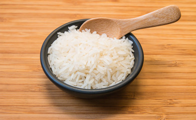 White rice in black bowl on wood plate with wood spoon