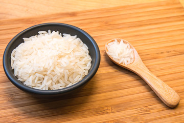White rice in black bowl on wood plate with wood spoon