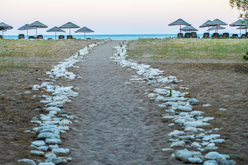 A rock marked road down to beach. There are sunshades and sunbeds and far away small horizontal area, sea is visible. Photo is taken in Antalya, Turkey