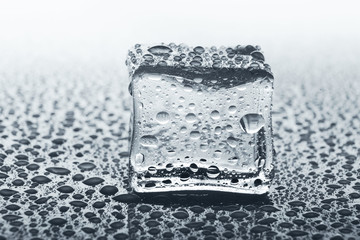 Transparent ice cube with reflection glass with water drops, monochrome