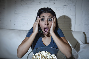 Naklejka premium latin woman sitting at home sofa couch in living room watching television scary horror movie
