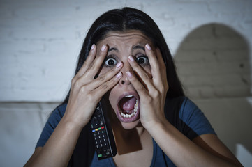 Fototapeta premium latin woman sitting at home sofa couch in living room watching television scary horror movie