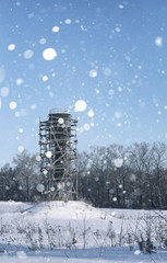 Scaffold around the water tower in field in front of forest in snow storm