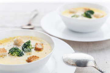 cheese soup with broccoli in a white plate on a white linen tablecloth