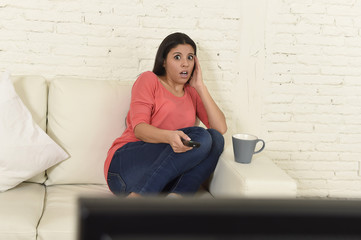 Naklejka premium latin woman sitting at home sofa couch in living room watching television scary horror movie