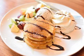 Stack of pancakes with fresh fruits, ice cream and whipped cream