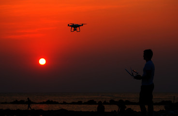 Man operating of flying drone quadrocopter at sunset