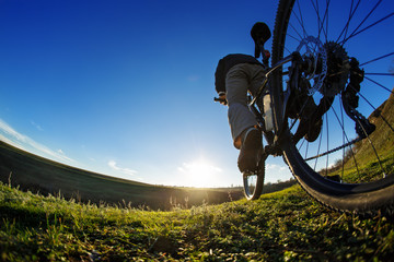 Fototapeta na wymiar Man on mountain bike rides on the trail on a beautiful sunrise. Bicycle wheel closeup.
