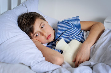 Kind mit Wärmflasche und Bauchschmerzen im Bett liegend