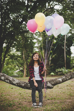 Young hipster woman sitting on tree branch with colorful of balloons in hand, Relaxing enjoy holiday.