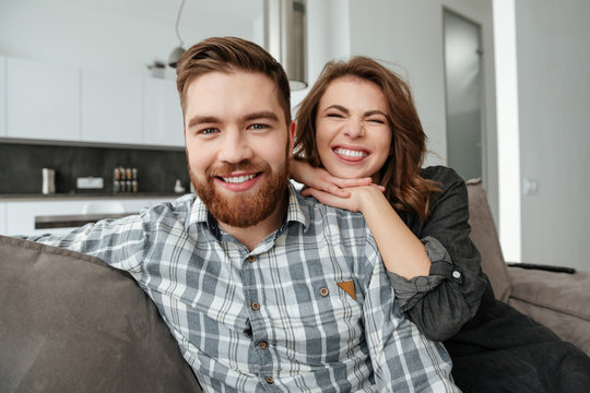 Young funny loving couple sitting on sofa indoors