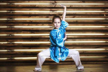 Pretty little girl in the room in sportswear for martial arts is Wushu