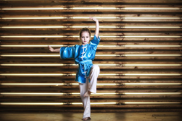Pretty little girl in the room in sportswear for martial arts is Wushu
