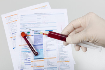 Hand mit Spritze und Blutprobe auf Analyseformular