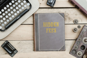 Hidden Fees on old book cover at office desk with vintage items