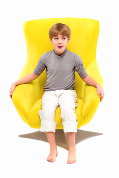 Portrait of cool young stylish boy sitting on yellow chair on light background