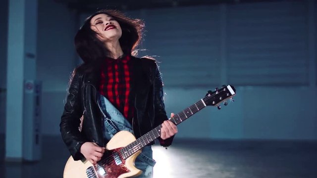 Young musician woman playing the guitar in hangar.