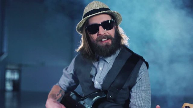 Man playing the bass guitar sitting in smoke while video production process.