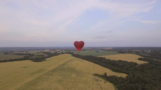 Red balloon in the shape of a wheat heart.Aerial view:Hot air balloon in the sky over a field in the countryside, beautiful sky and sunset.Aerostat fly in the countryside. 4K video,ultra HD.