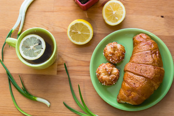 Tea with lemon and croissant for fresh spring breakfast on wooden table