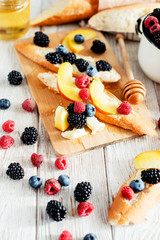 sweet snack , bruschetta with berries and fruits , blueberries , raspberries, blackberries and peaches , with butter and honey on wooden background