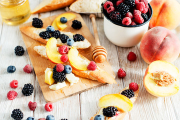 sweet snack , bruschetta with berries and fruits , blueberries , raspberries, blackberries and peaches , with butter and honey on wooden background
