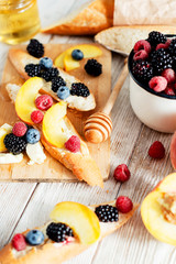 sweet snack , bruschetta with berries and fruits , blueberries , raspberries, blackberries and peaches , with butter and honey on wooden background