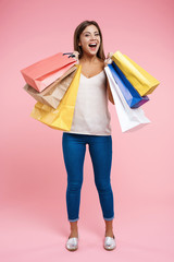 Happy young woman holding shopping bags staying on pink background