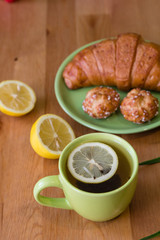 Tea with lemon and croissant for fresh spring breakfast on wooden table