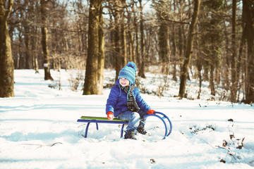 Fototapeta na wymiar Little boy enjoying a sleigh ride. Child sledding. Toddler kid riding a sled. Children play outdoors in snow. Kids sled in winter park. Outdoor active fun for family vacation.