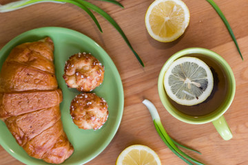 Tea with lemon and croissant for fresh spring breakfast on wooden table