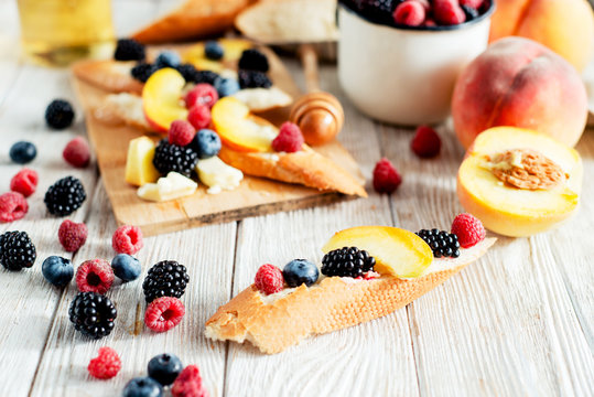 sweet snack , bruschetta with berries and fruits , blueberries , raspberries, blackberries and peaches , with butter and honey on wooden background