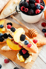 sweet snack , bruschetta with berries and fruits , blueberries , raspberries, blackberries and peaches , with butter and honey on wooden background