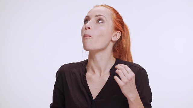 Middle-aged Caucasian woman in dark brown shirt and colored orange hair plucking imaginary grapes and eating them on white background in slowmotion