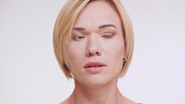 Close up footage of afraid Caucasian female with blonde hair standing on white background in shock in slowmotion