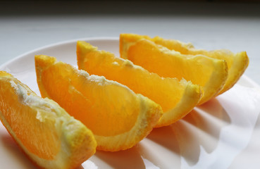 Close view of orange slices on a white plate surface and a dark shadowy background