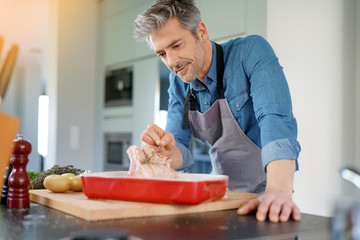 Mature man in kitchen cooking dish for dinner - obrazy, fototapety, plakaty