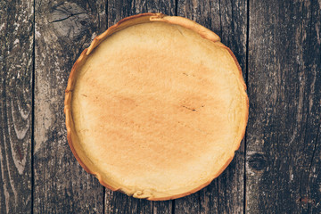 Cooked base for homemade pie on rustic wooden background.