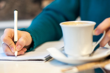 female hand signing in notebook and drinking coffee, on bright background
