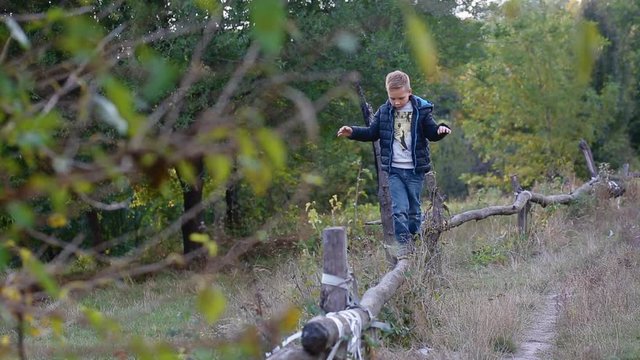 Little boy walk and balance on the log outdoor trying not to fall down.