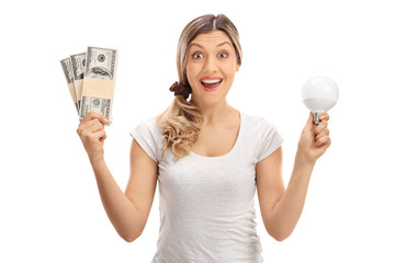 Delighted woman holding bundles of money and LED light bulb