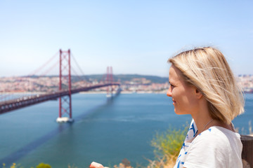 Female traveler standing next to the statue of National Sanctuary of Christ the King and enjoys panoramic views of Lisbon and the bridge of April 25.