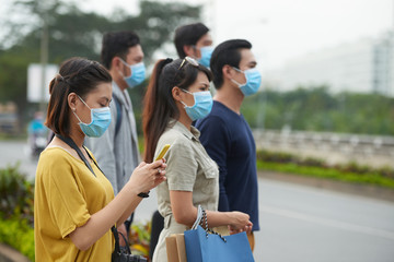 Profile view of two Asian women and three Asian men in protective masks standing on roadside of modern city