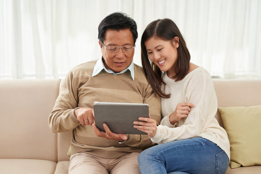 Asian family of two relaxing in living room and watching their favorite program on digital tablet