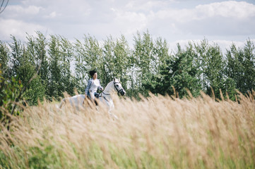 Happy brunette woman riding her white stallion, having fun at the summer field