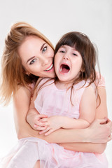 portrait of blonde mom and sweet little daughter in pink dresses