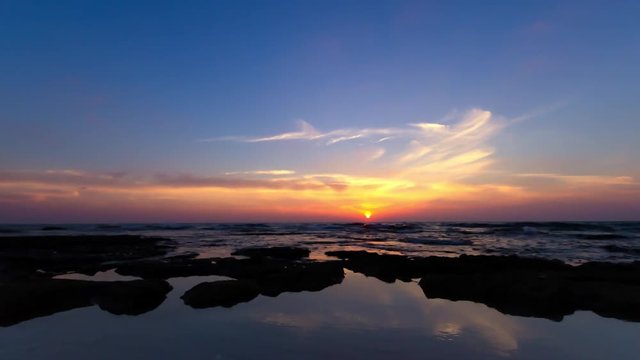 time lapse of clouds crossing the amazing sky over the sea or ocean at sunset. transition from day to night. The clouds cross slowly from left to right colored yellow orange purple blue